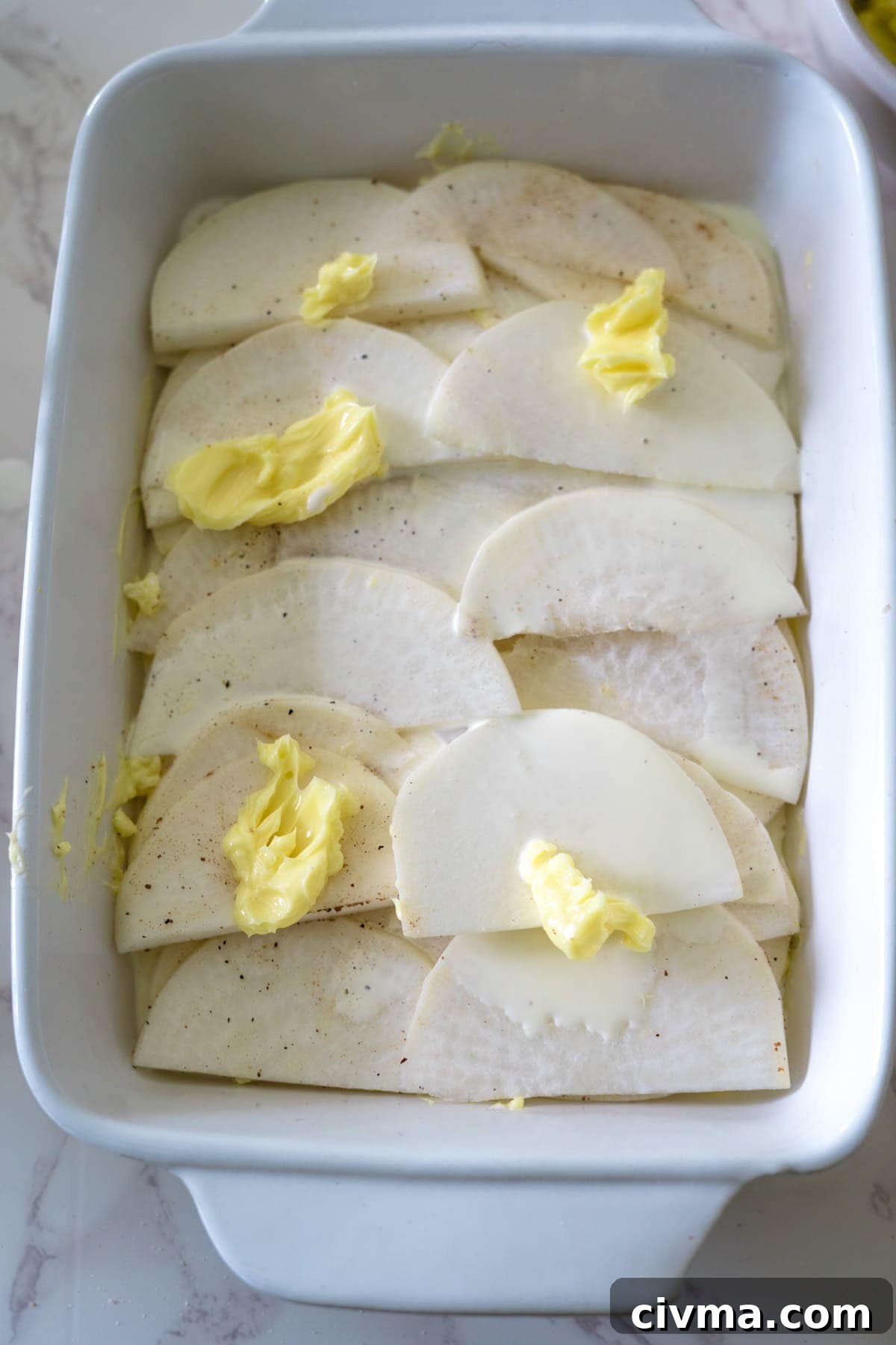 Sliced potatoes in a baking dish with butter, baked to perfection for a delicious turnip gratin.