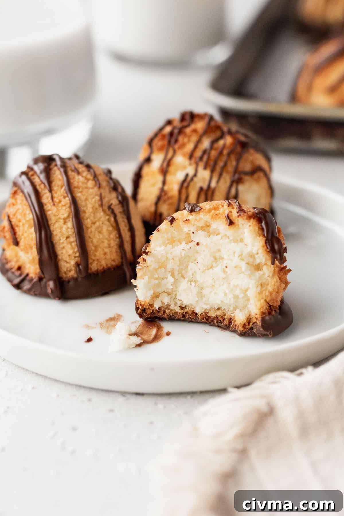 Three gluten-free vegan macaroons on a white plate, one with a bite taken out.