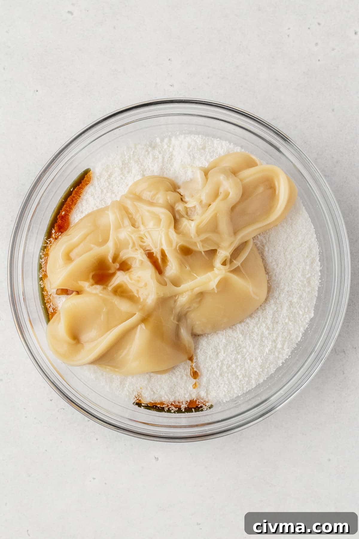 Coconut, vegan condensed milk, and vanilla extract in a glass bowl.