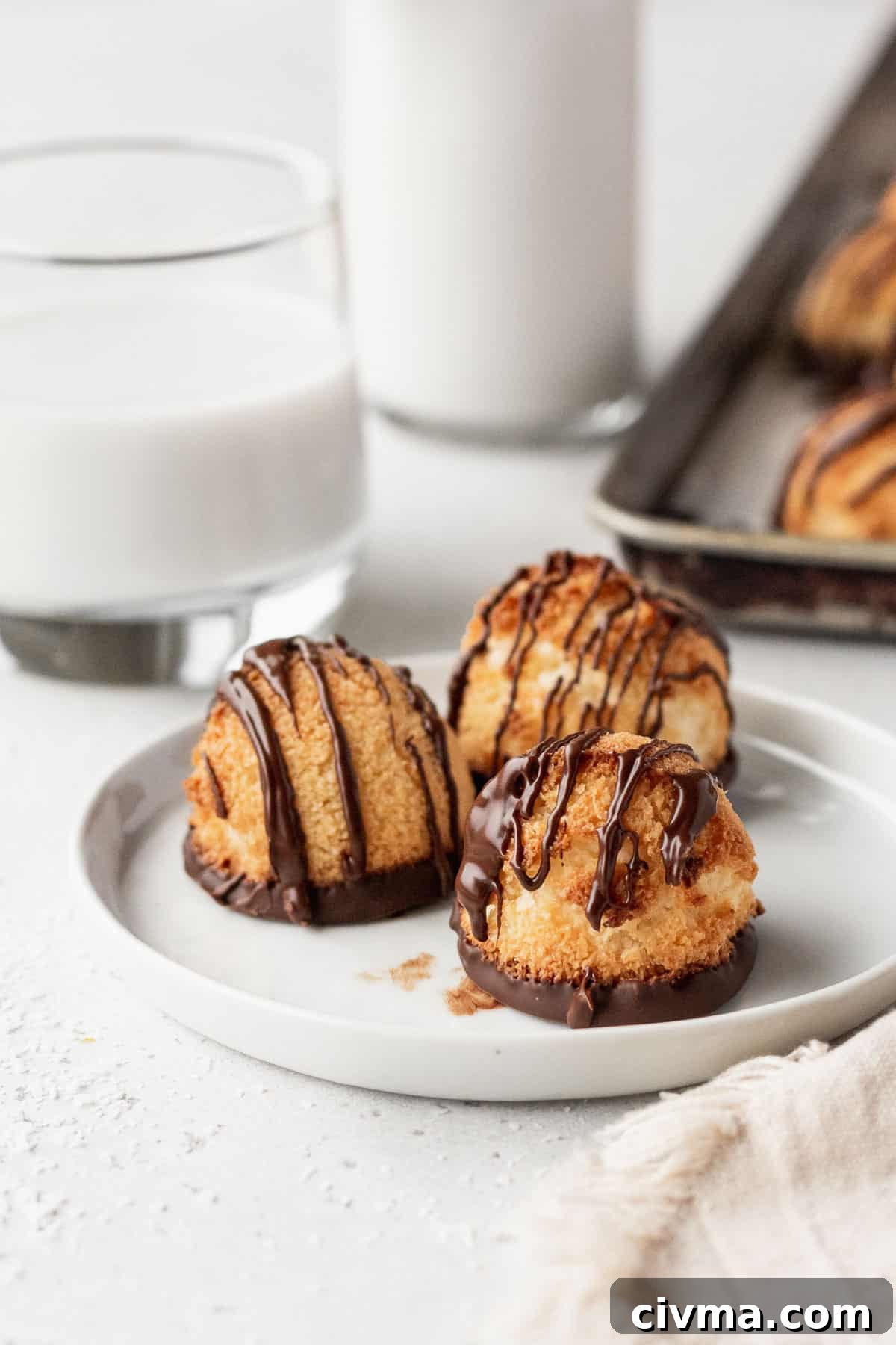 Three chocolate drizzled coconut macaroons on a white plate with a glass of milk.