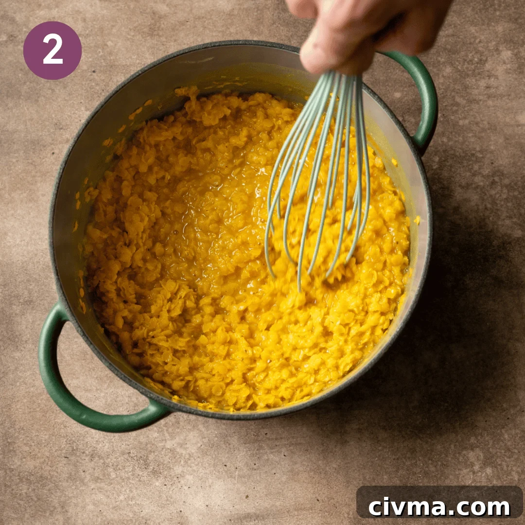 Person stirring cooked lentils with a whisk in the pot.
