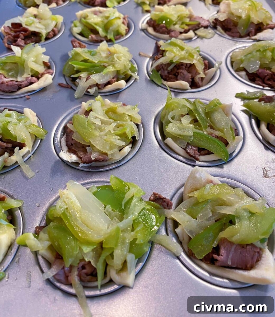 Philly Cheesesteak Bites Recipe 8 Mini Philly Cheesesteaks in a mini-muffin pan with cooked veggies on top of each one.