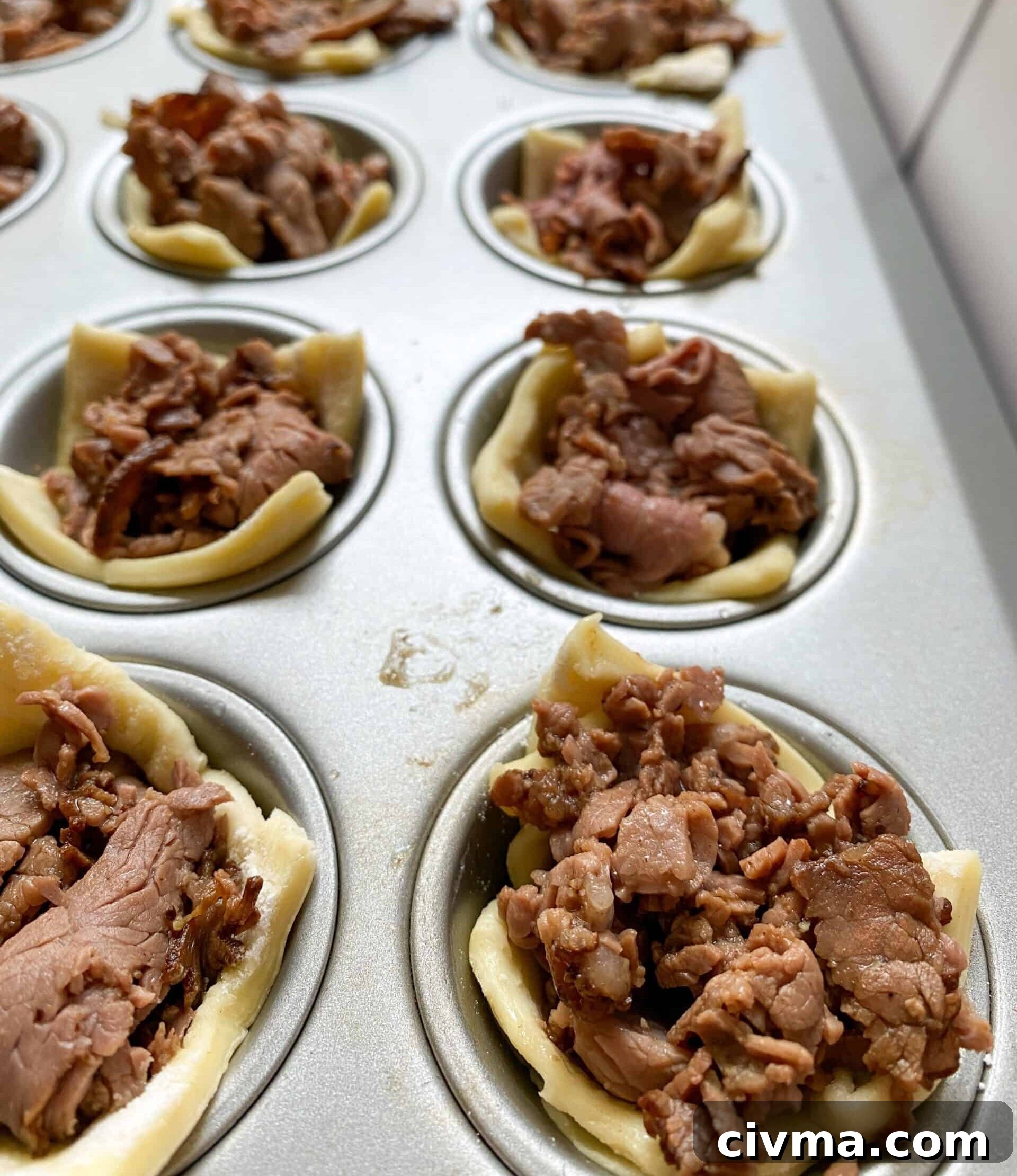 Philly Cheesesteak Bites Recipe 10 Mini muffin cups with cooked roast beef and puffed pastry in each one.