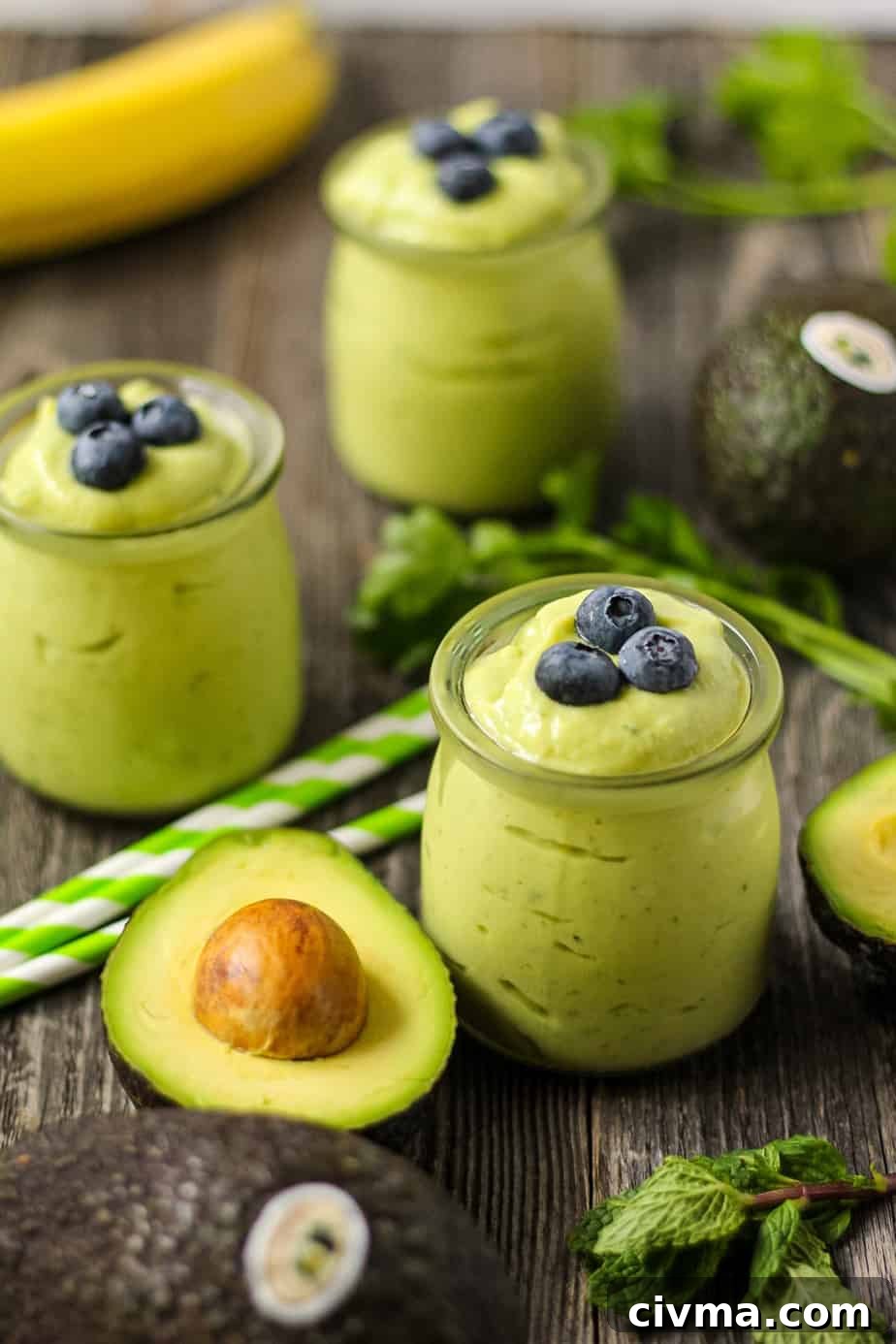 side shot of tropical avocado smoothies with fresh avocados in perimeter of shot