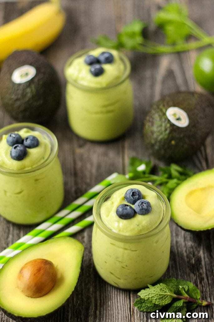 side shot of tropical avocado smoothies on wooden surface with fresh avocados in perimeter of shot