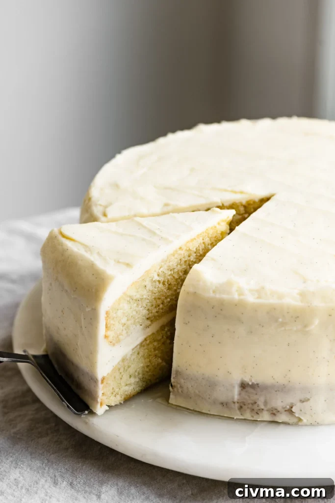 Two layer vanilla cake with vanilla bean frosting on a plate with a slice being pulled out on a pie server.