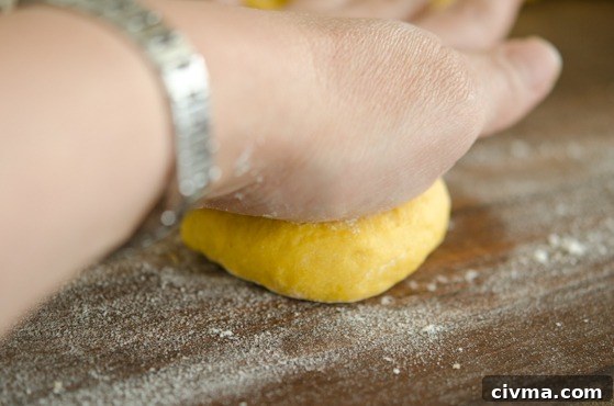 Flatten a piece of pumpkin dinner roll dough with a hand.