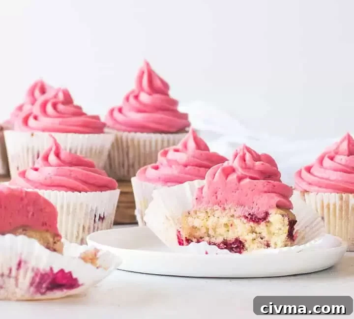 raspberry cupcake cut in half sitting on a plate with more cupcakes behind it
