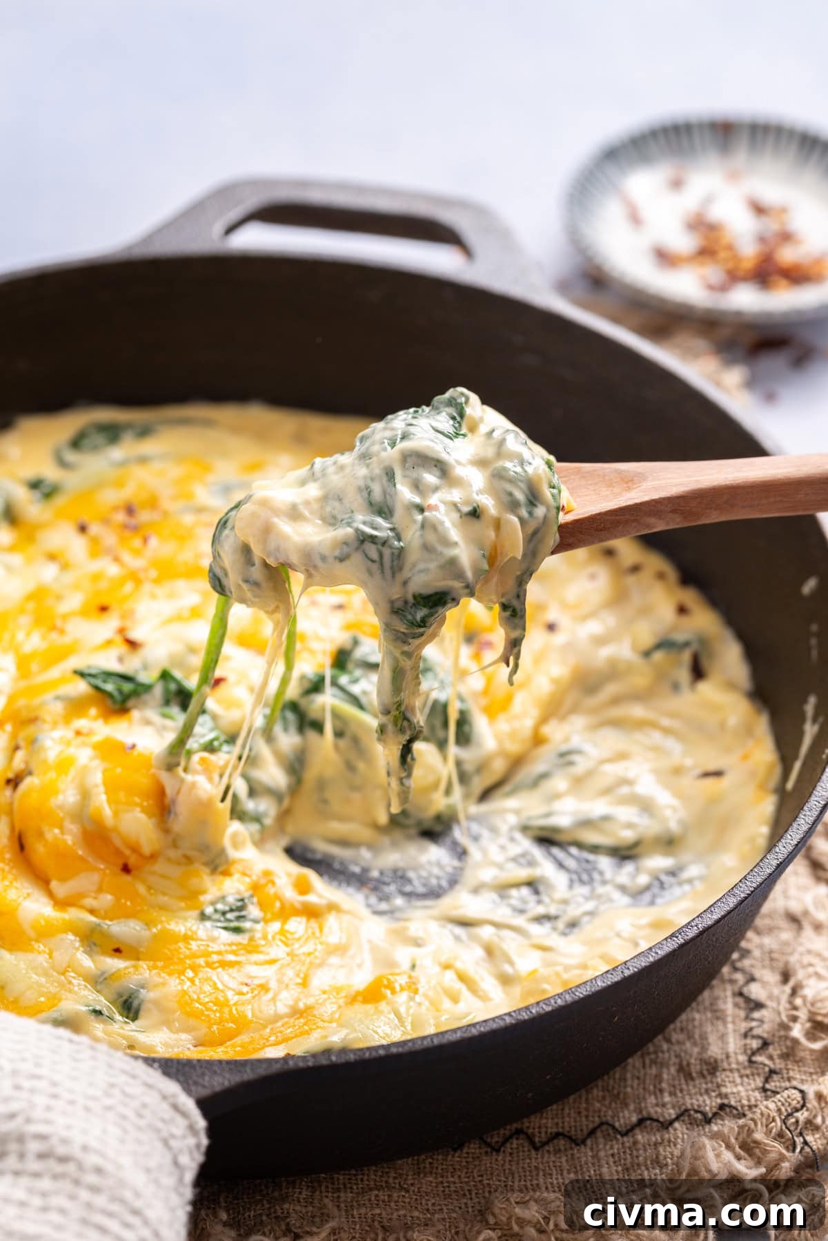 An image of creamed spinach in a cast iron skillet. A wooden spoon with a scoop of creamed spinach hovering over it.
