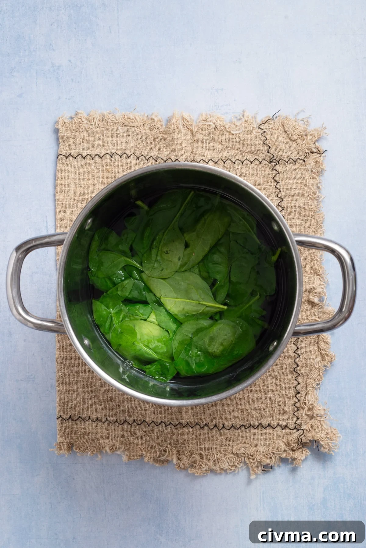 An overhead image of fresh spinach being blanched in a pot.