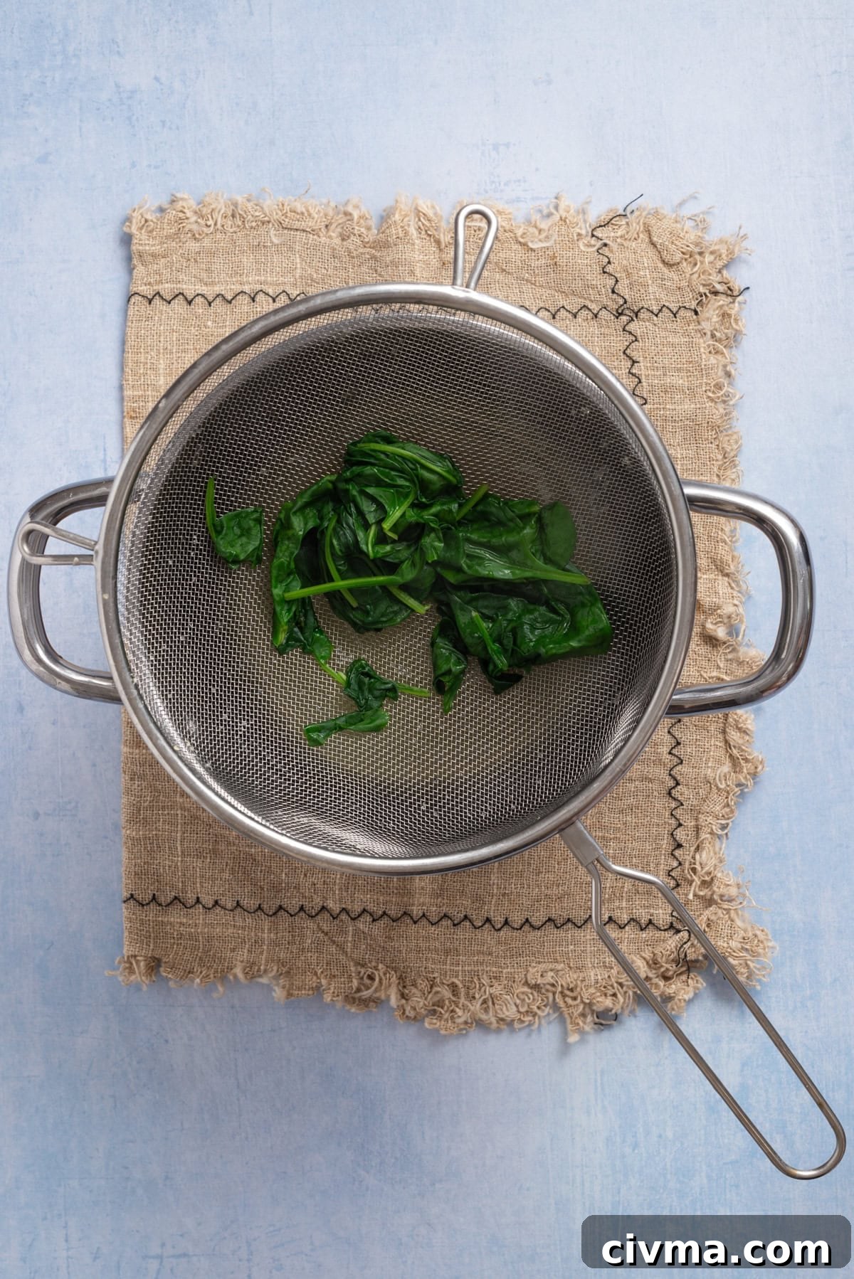 An overhead image of fresh spinach on a colander after blanching.