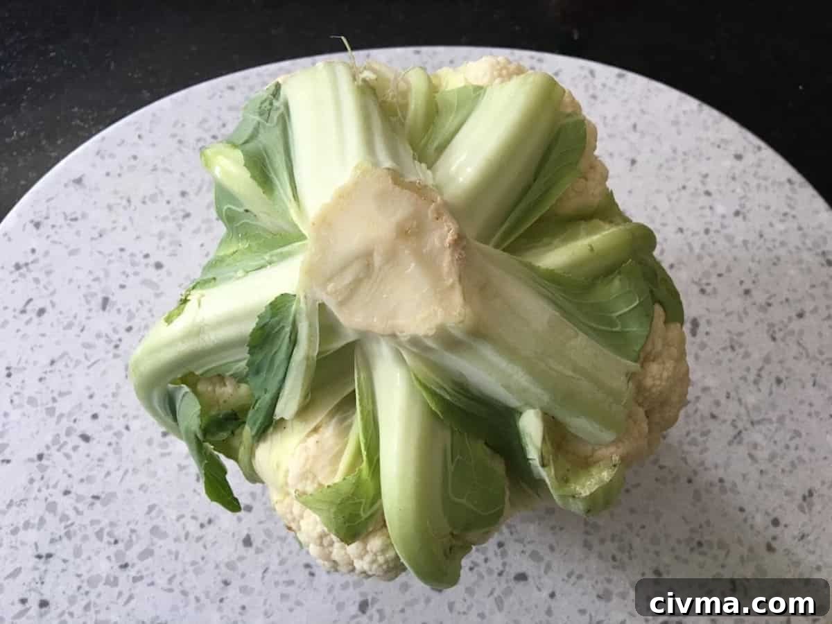 A head of cauliflower upside down on a cutting board showing the stem and leaves.
