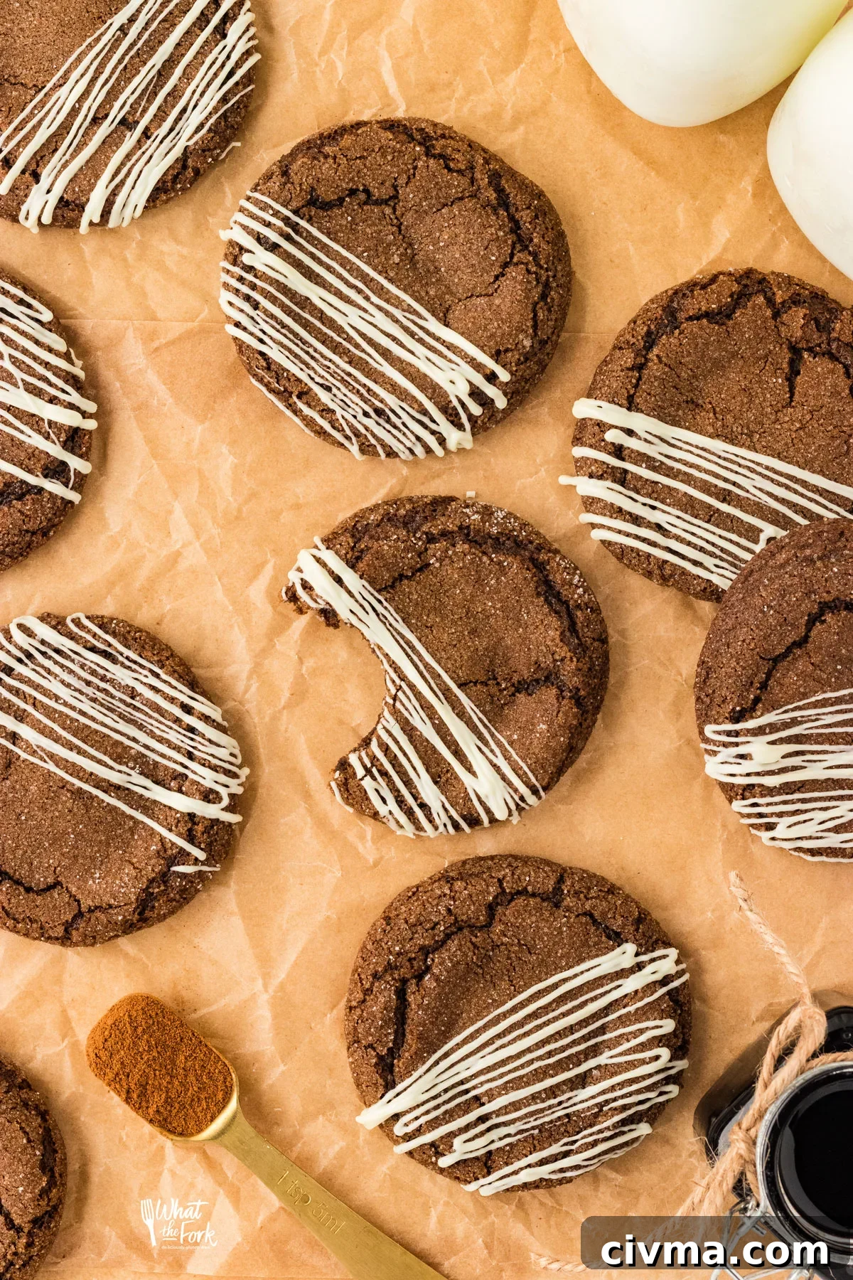 overhead shot of baked gluten free ginger cookies drizzled with white chocolate on top of brown parchment paper. One cookie has a bite taken from it.