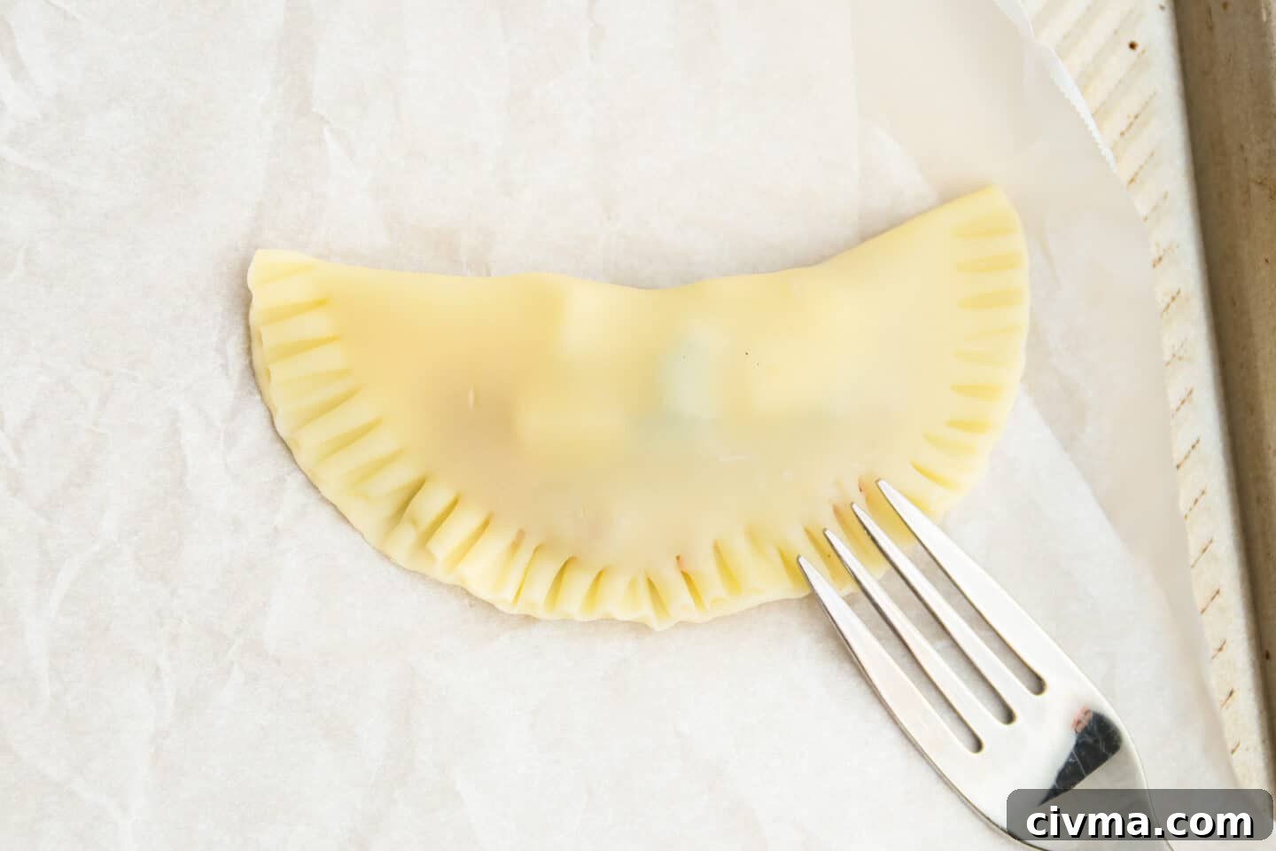 This is a picture of an empanada being sealed with a fork.