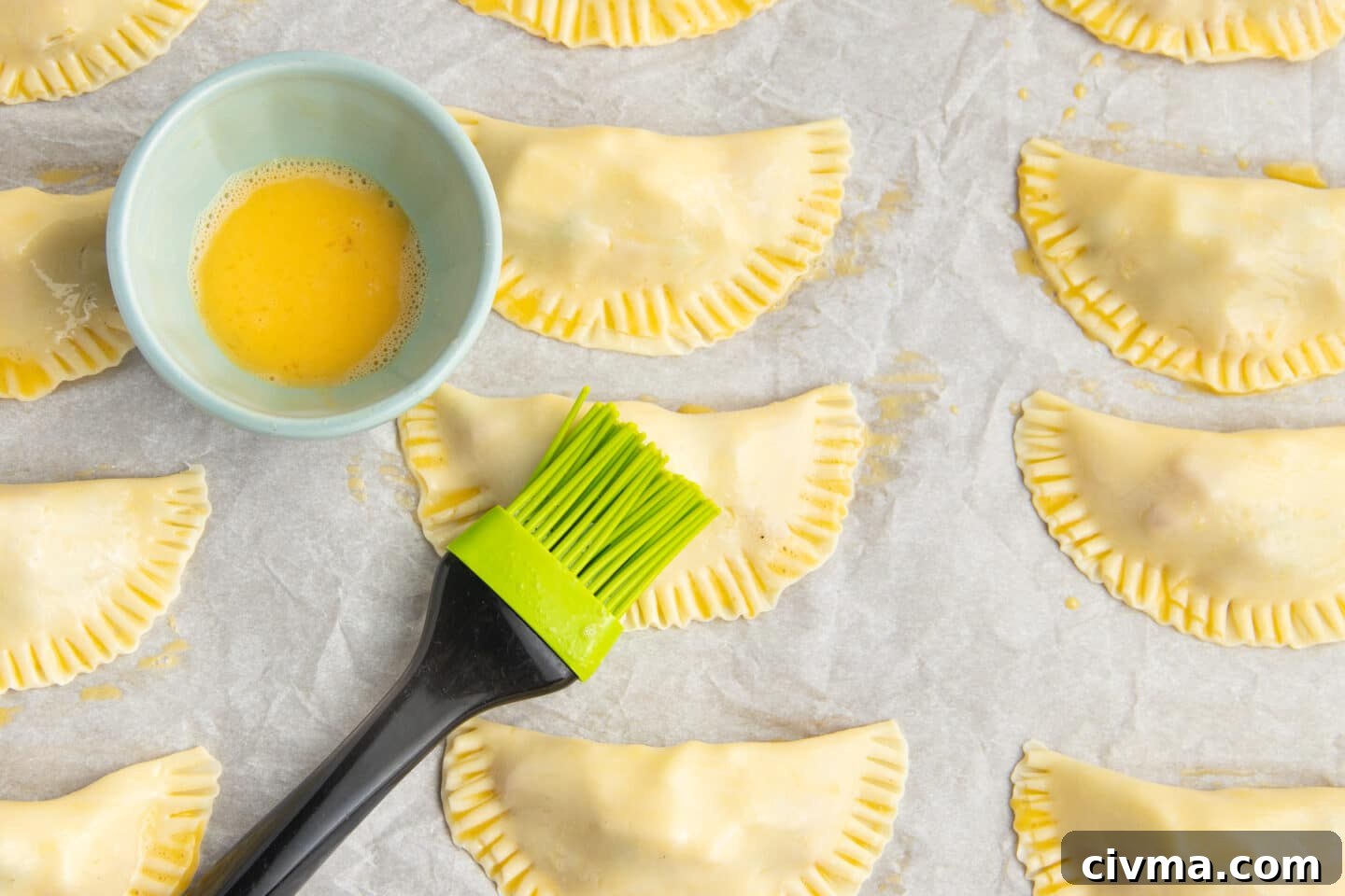 This is a picture of empanadas being brushed with a beaten egg and basting brush.