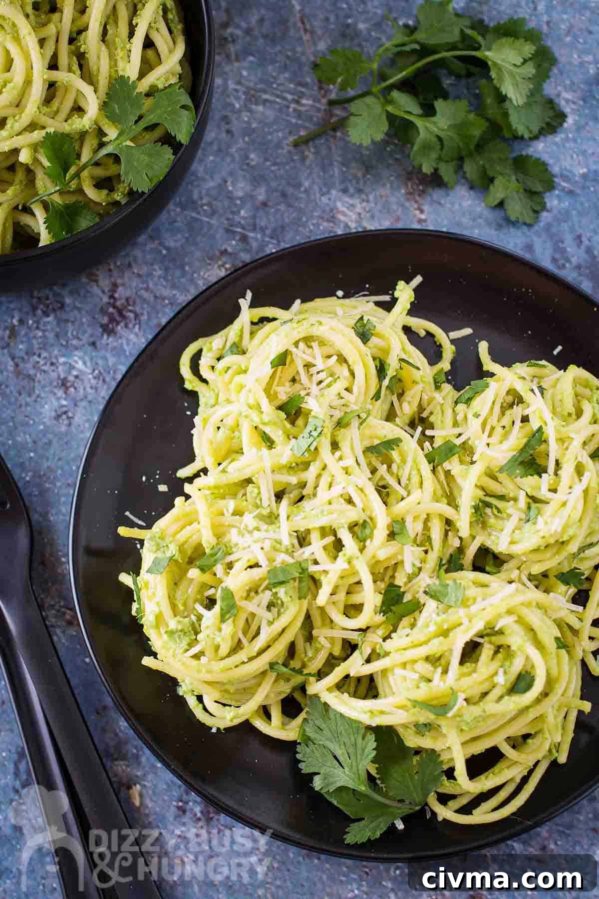 Green Spaghetti with Creamy Poblano Sauce 2 Overhead shot of green spaghetti garnished with parmesan and parsley leaves on a black plate with a parsley bundle on the side.