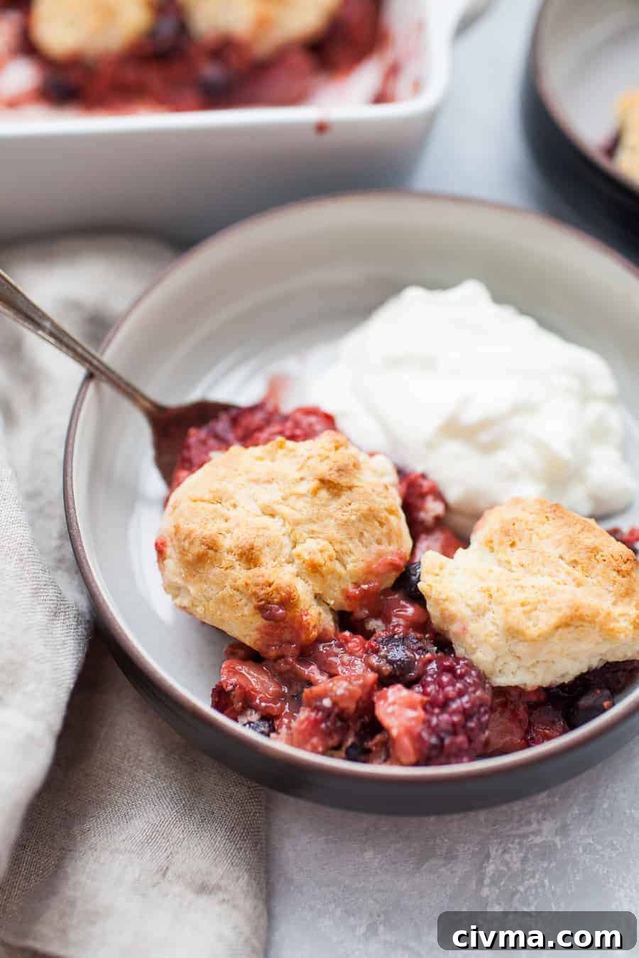 Close up of mixed berry cobbler in a black bowl with yogurt, berries, and an antique spoon.