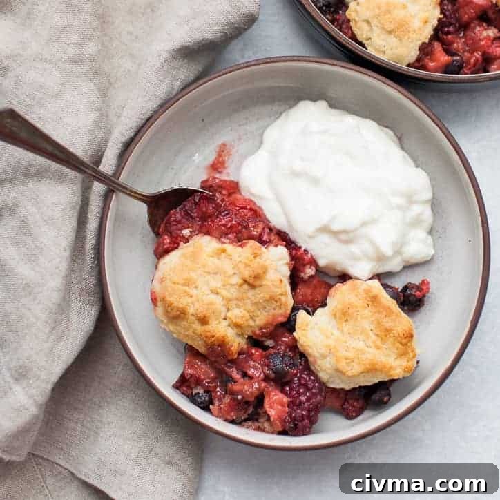 Mixed berry cobbler in a black bowl with yogurt and a spoon.