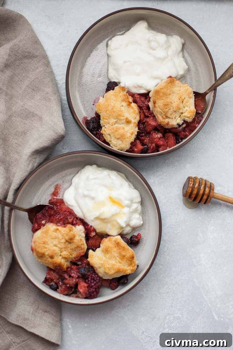 Overhead view of two black bowls filled with mixed berry cobbler and yogurt.