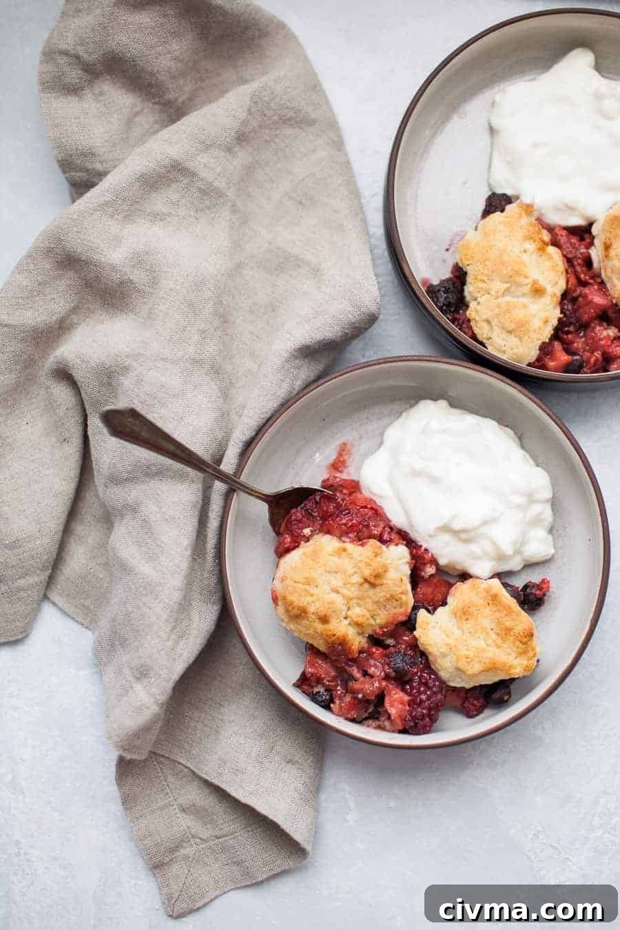 Two bowls of mixed berry cobbler with yogurt and visible blueberries, strawberries, and raspberries.