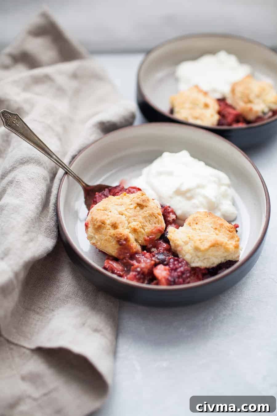 Close up of a black bowl of mixed berry cobbler with yogurt and a spoon.