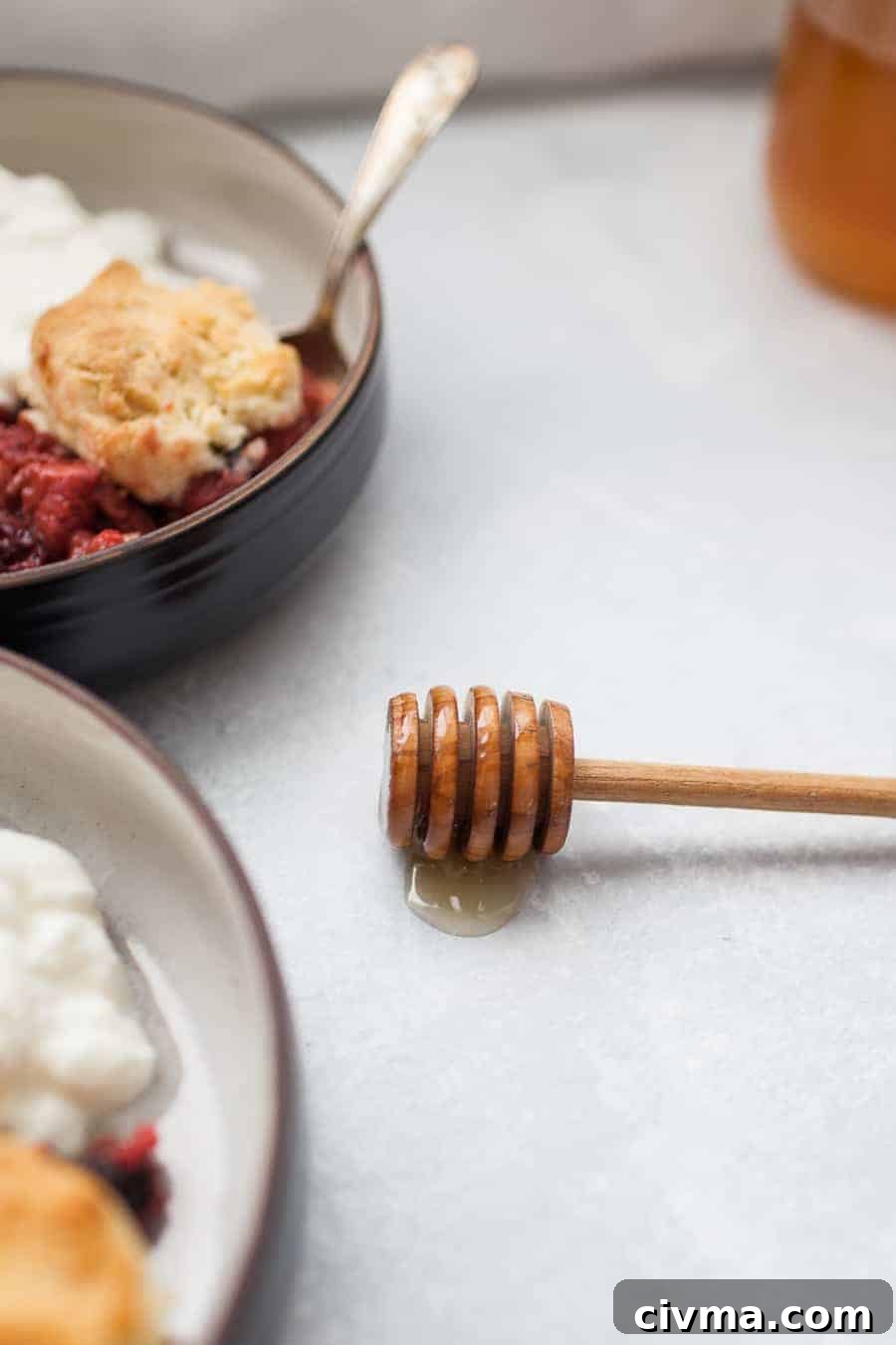 Honey dipper in a small pool of honey with bowls of cobbler in the background.