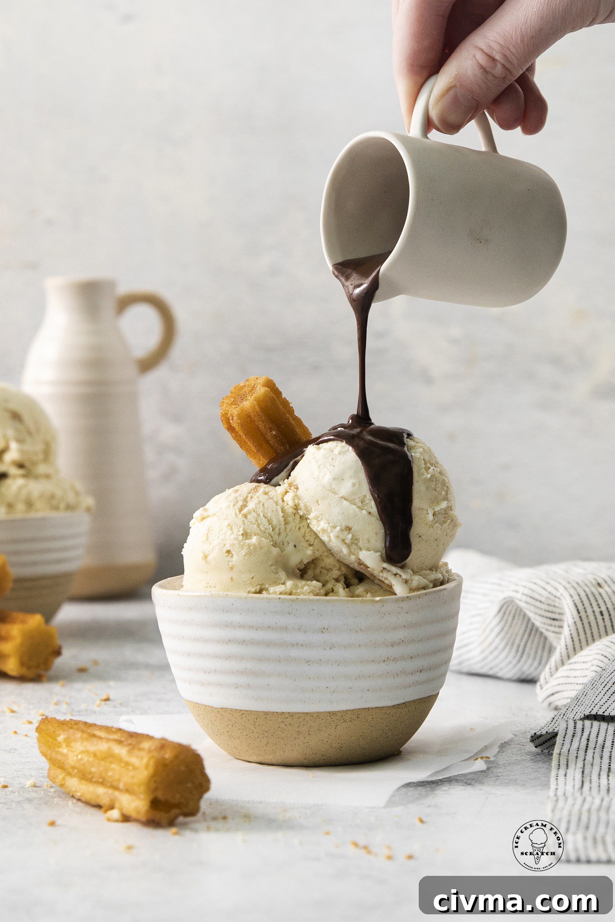 a bowl of churro ice cream with a churro stuck into it and chocolate sauce being poured over.
