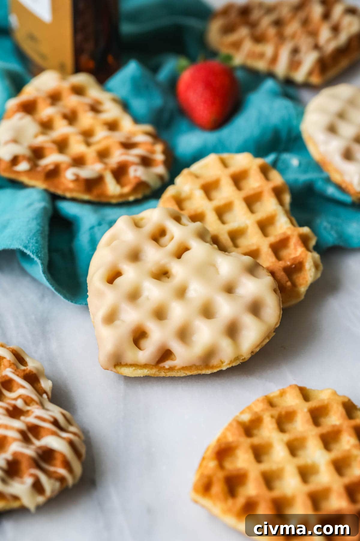 Waffle cookie that's been dipped in glaze surrounded by other cookies that are drizzled with glaze.
