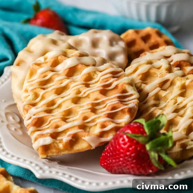 Heart shaped waffle cookies with a drizzled maple glaze on a white plate with a strawberry.