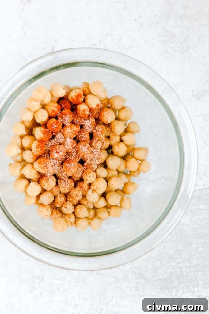 Seasoning sprinkled on chickpeas in a glass mixing bowl.