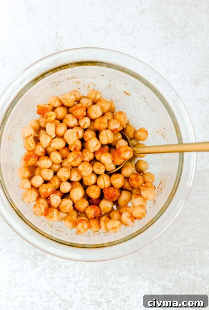 Chickpeas and seasoning mixed together in glass mixing bowl.
