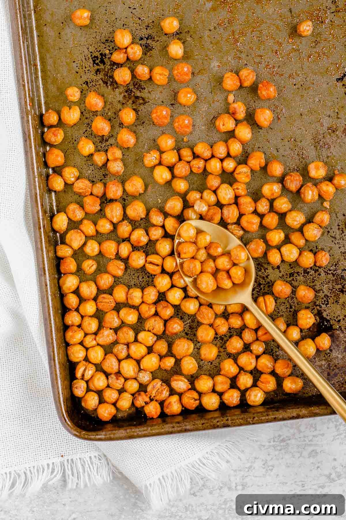 Oven roasted chickpeas on a baking sheet with a gold spoon.