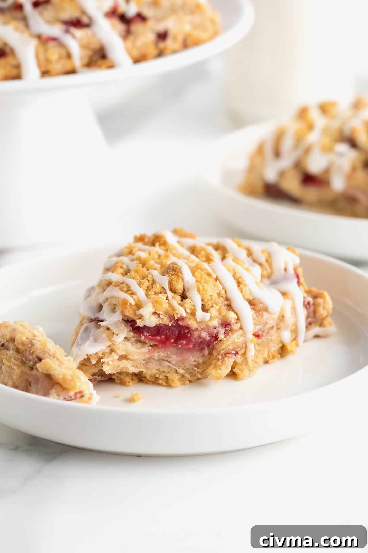A strawberry streusel scone with icing on a white plate.