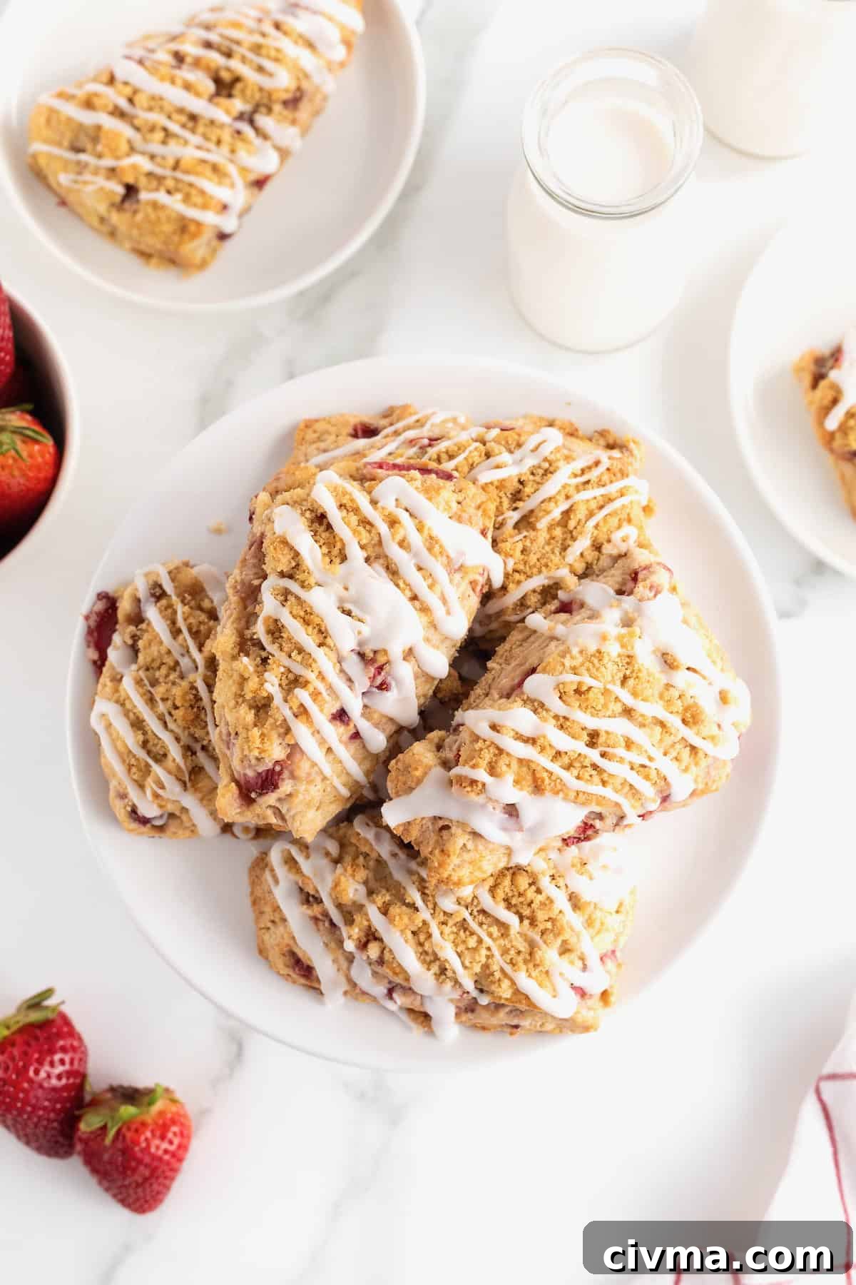 Five strawberry streusel scones drizzled with icing on a white serving platter.