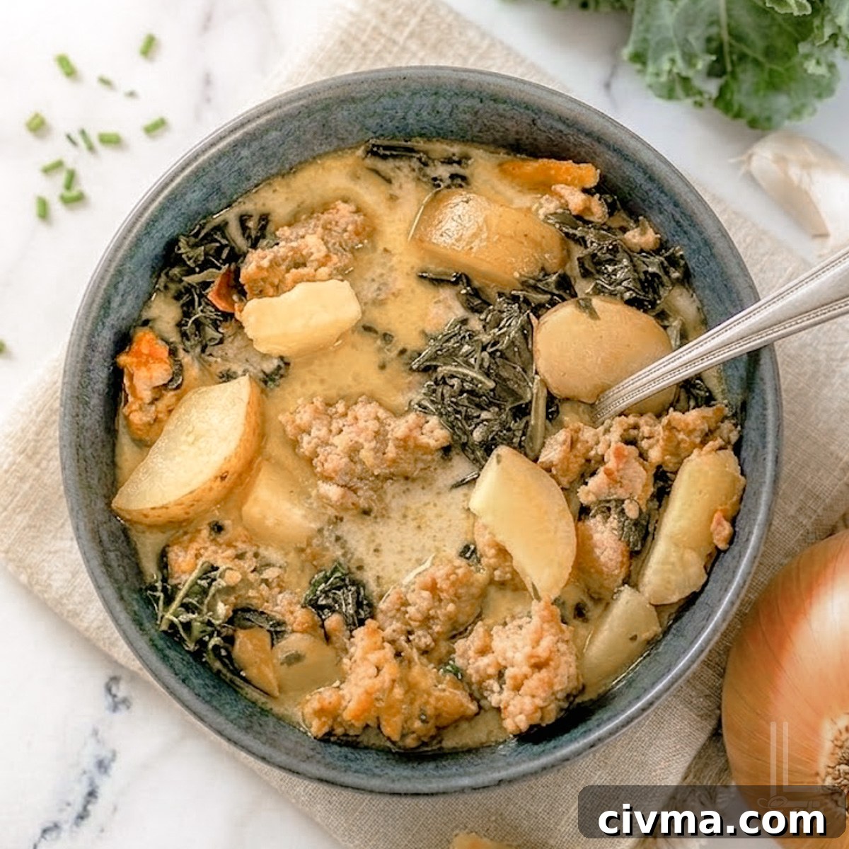 bowl of instant pot zuppa toscana, with potatoes, kale, and sausage in a creamy soup base, next to an onion, garlic, and kale.