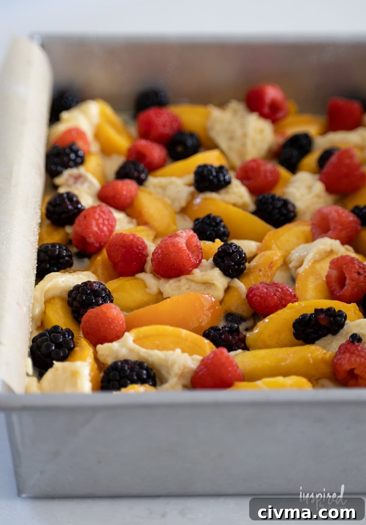 fruit on top of unbaked Nectarine and Berry Buckle in a cake pan.