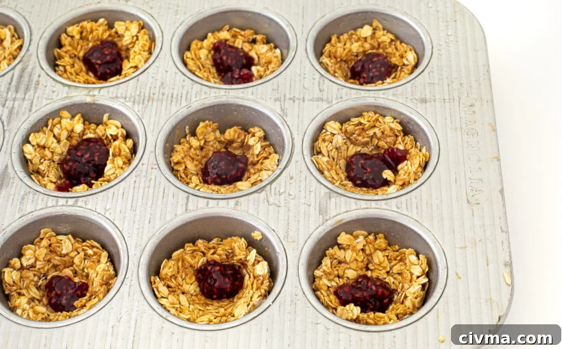 Oat cups in a muffin tin topped with dollops of raspberry jam.
