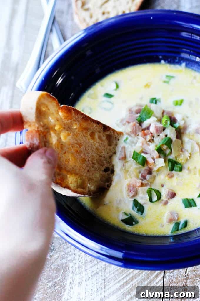 ham and cheese soup with scallion in blue bowl with hand dunking the bread in the soup