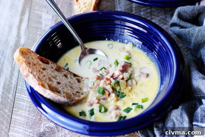 ham and cheese soup in blue bowl with scallion, bread and spoon inside, vertical shot