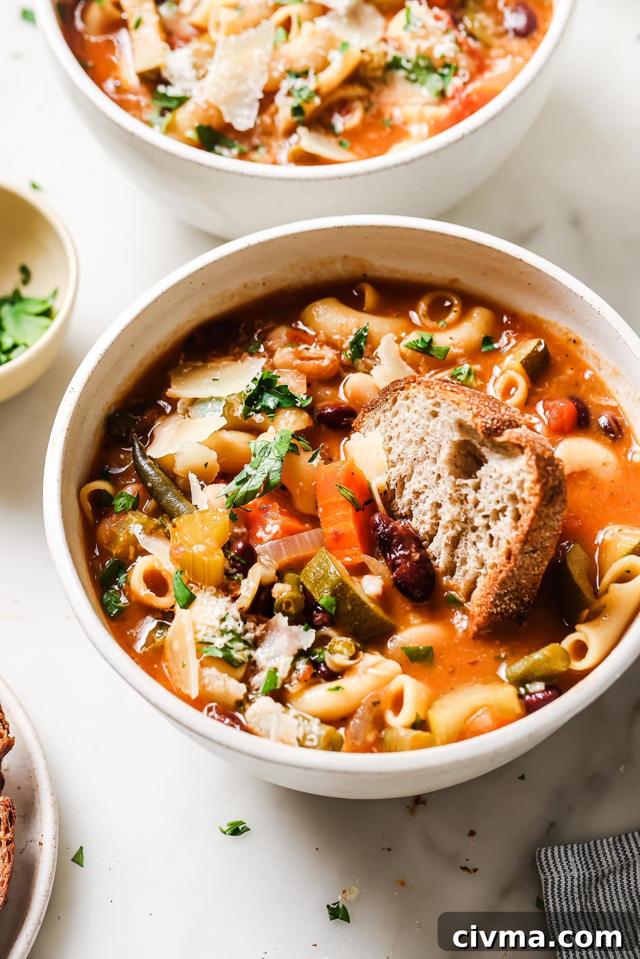 A bowl of Minestrone Soup with a slice of fresh bread dipped into it. 