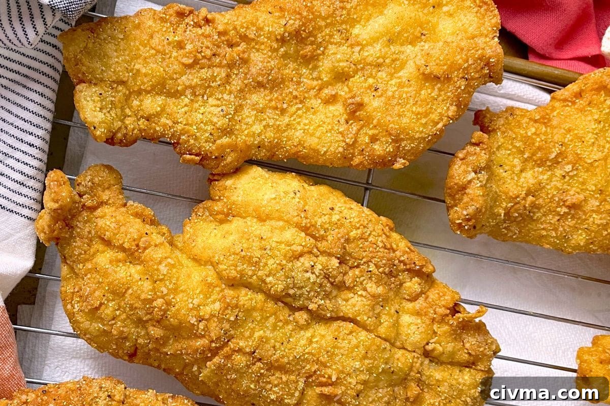 Golden-brown fried fish fillets resting on a cooling rack, showcasing a crunchy texture and savory seasoning.