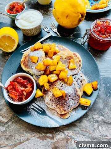ricotta pancakes topped with chopped pineapple and a small serving dish with jam on a black plate