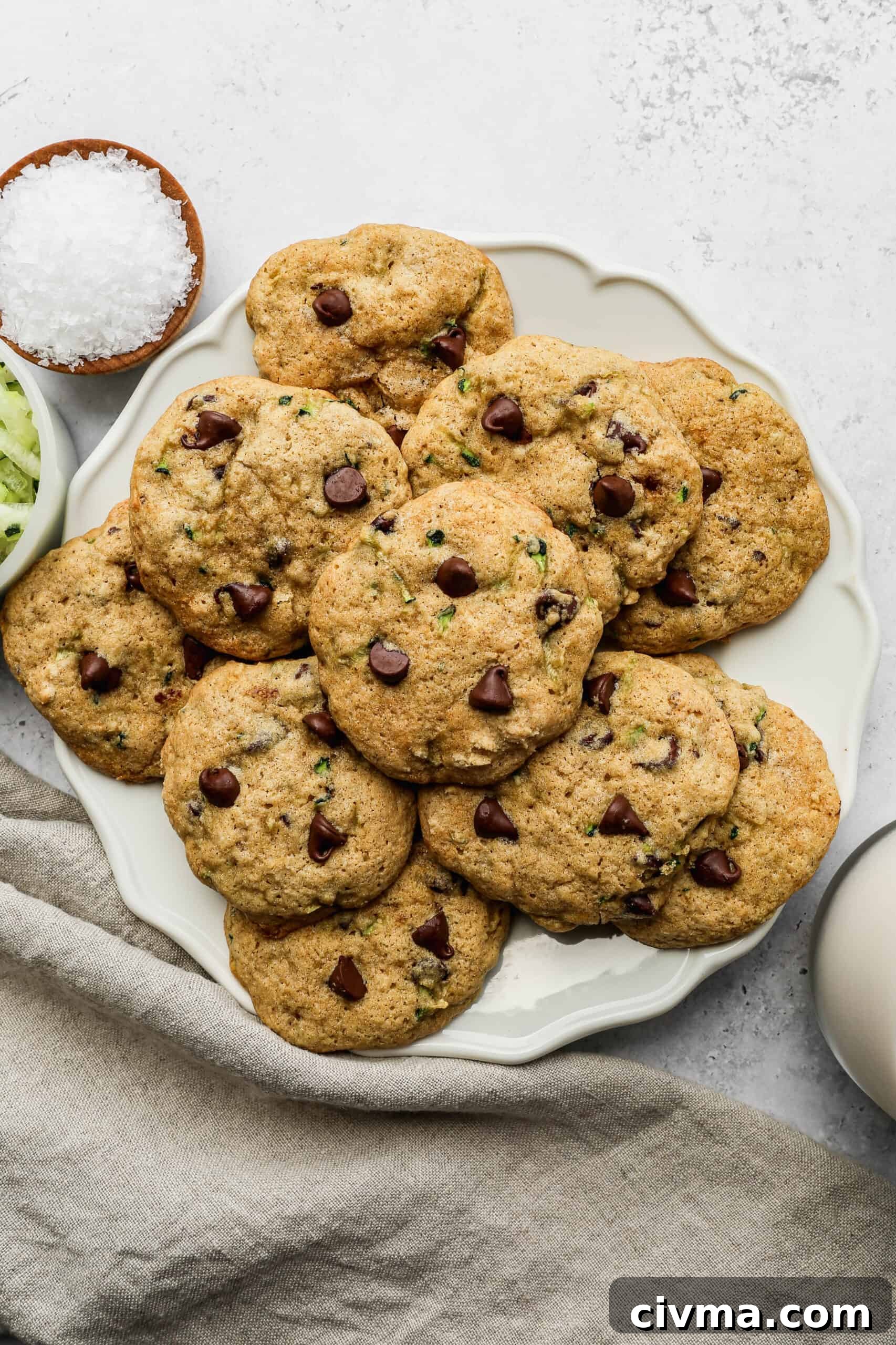 a white plate of gluten free zucchini chocolate chip cookies next to a small white bowl of shredded zucchini.