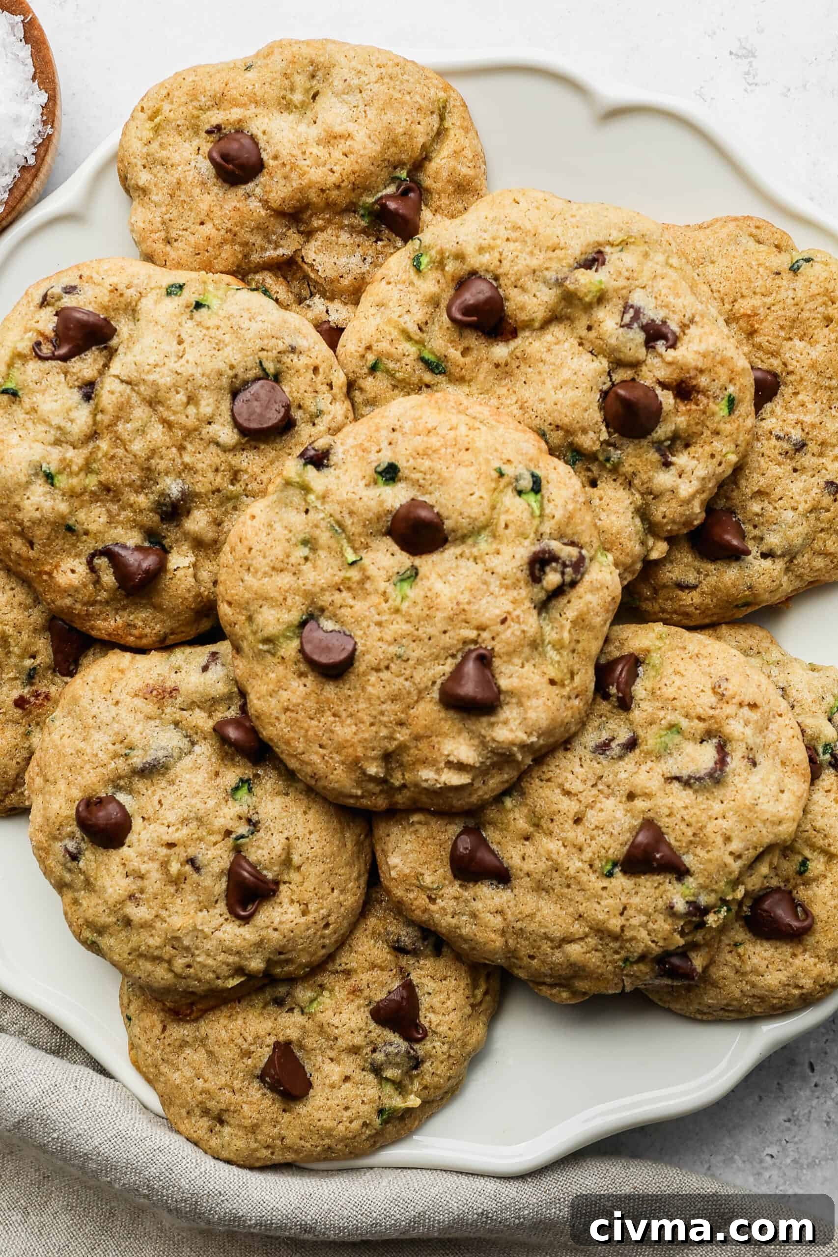 a white plate of gluten free zucchini chocolate chip cookies next to a small wooden bowl of coarse sea salt.