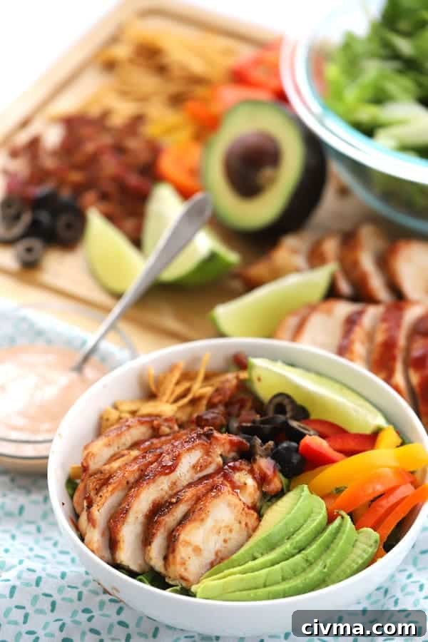 BBQ grilled chicken salad in a serving bowl with more fresh ingredients in the background.