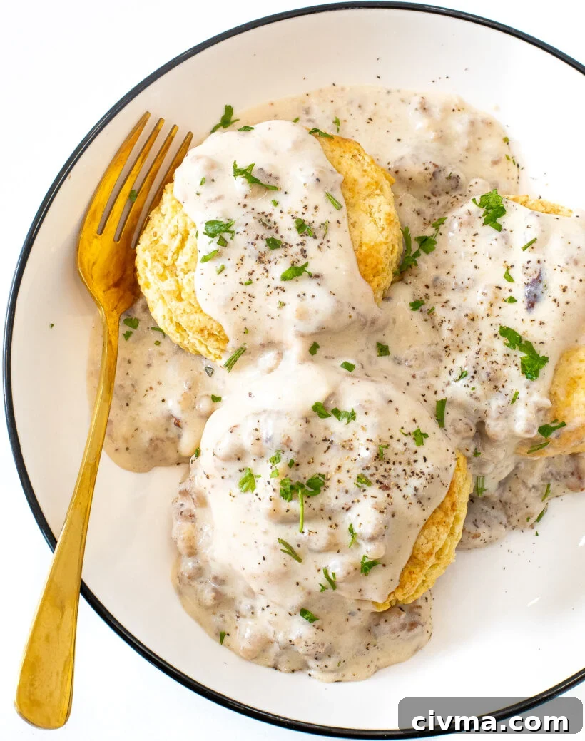3 fluffy biscuits topped with sausage gravy on a white plate with a gold spoon.