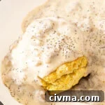 Sausage gravy poured on top of a biscuit on a white plate.