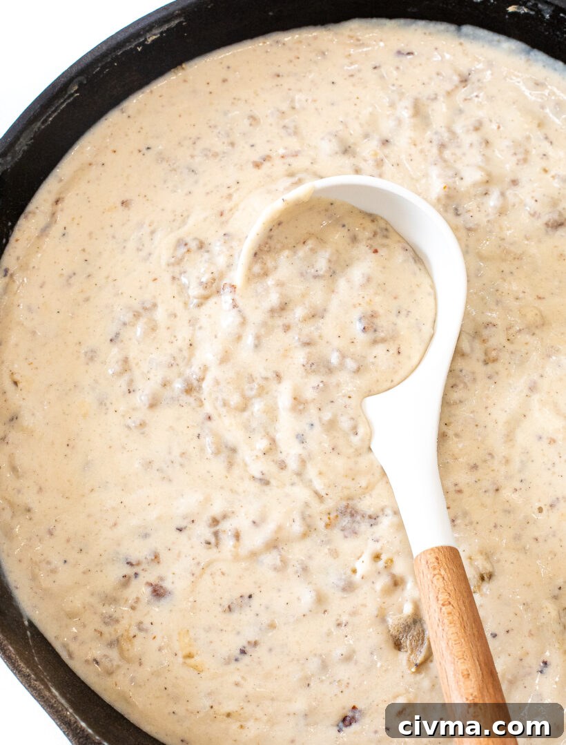 A white and wood spoon in a pan full of sausage gravy.