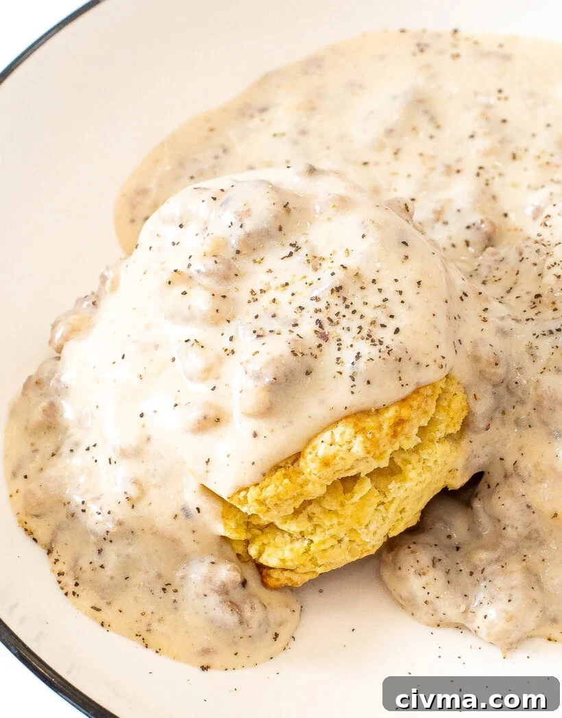 A fluffy biscuit topped with sausage gravy on a white plate.
