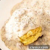 Sausage gravy poured on top of a biscuit on a white plate.